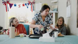 a nurse assisting to women in a dining room at a skilled nursing facility