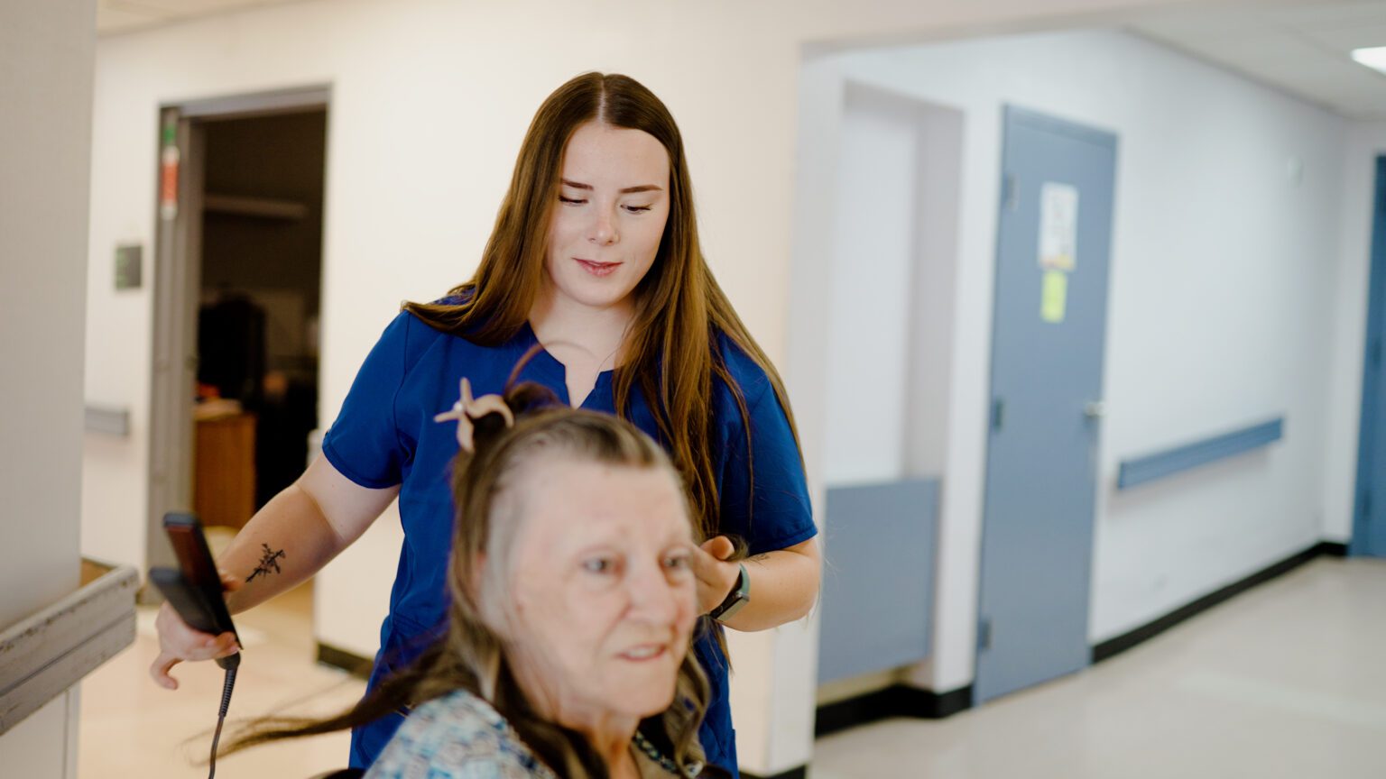 A woman gets her hair done by a stylist at a skilled nursing facility