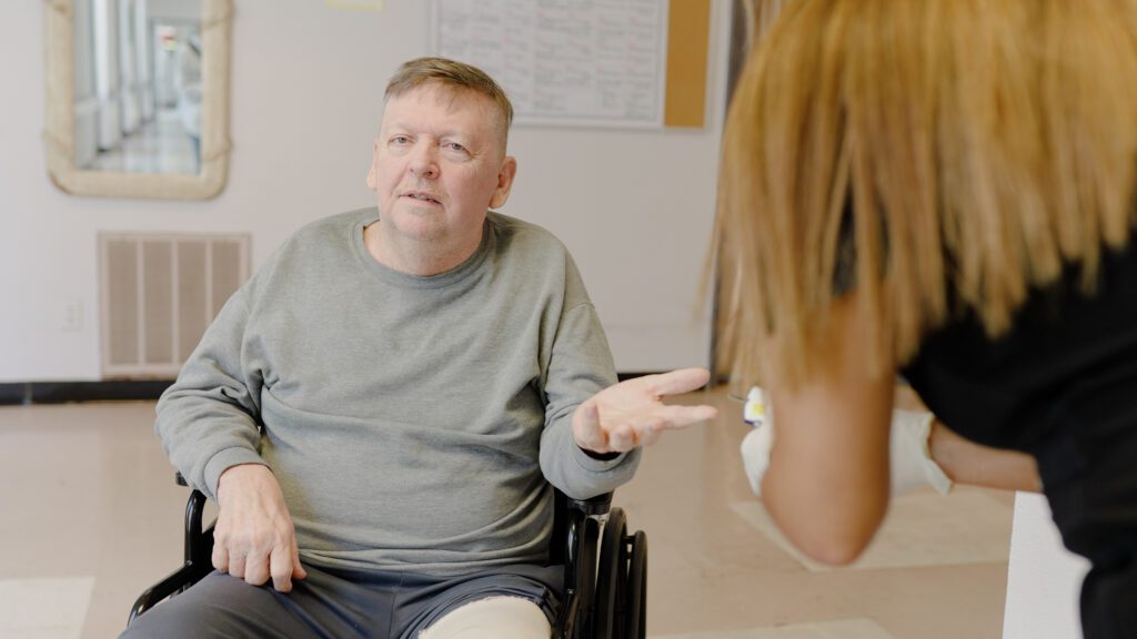 A man receiving short-term rehab talks to a nurse at a skilled nursing facility